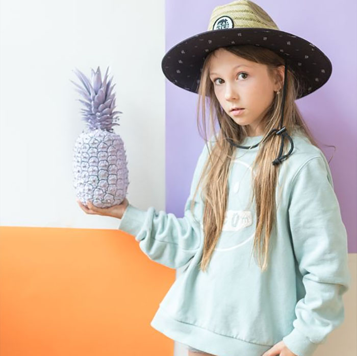 Chica con sombrero de Headster sosteniendo una piña morada | Marcas de ropa para niños